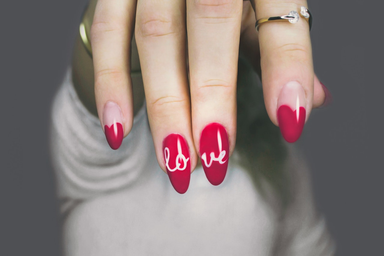 a woman with red nails with nail art that reads "love"