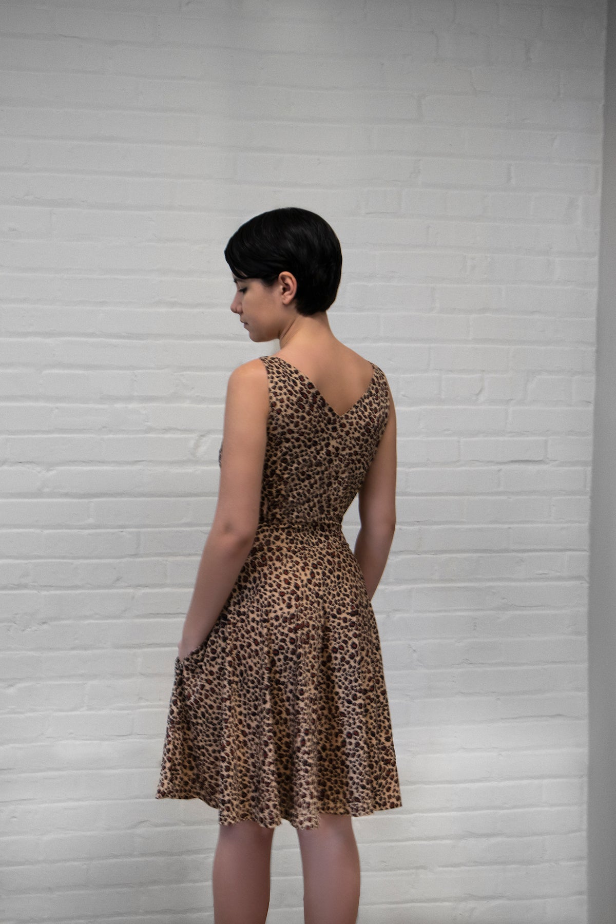 a model wearing a leopard animal print dress with a v-neck and no sleeves (back view)